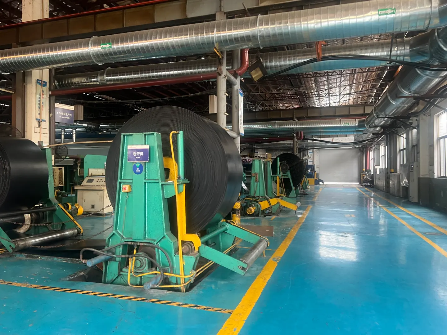Belt winding equipment and a large black belt roll beside a workshop aisle